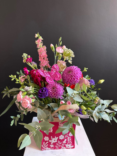 Pretty in Pink - A vibrant floral arrangement in a decorative gift bag, beautifully arranged in bright pink and purple tones with seasonal flowers and foliage.